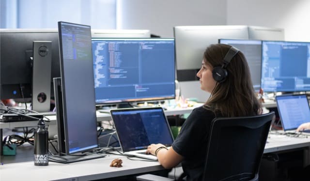 Chica con audífonos programa con lenguaje Clojure en computadora disfrutando trabajar en Nu
