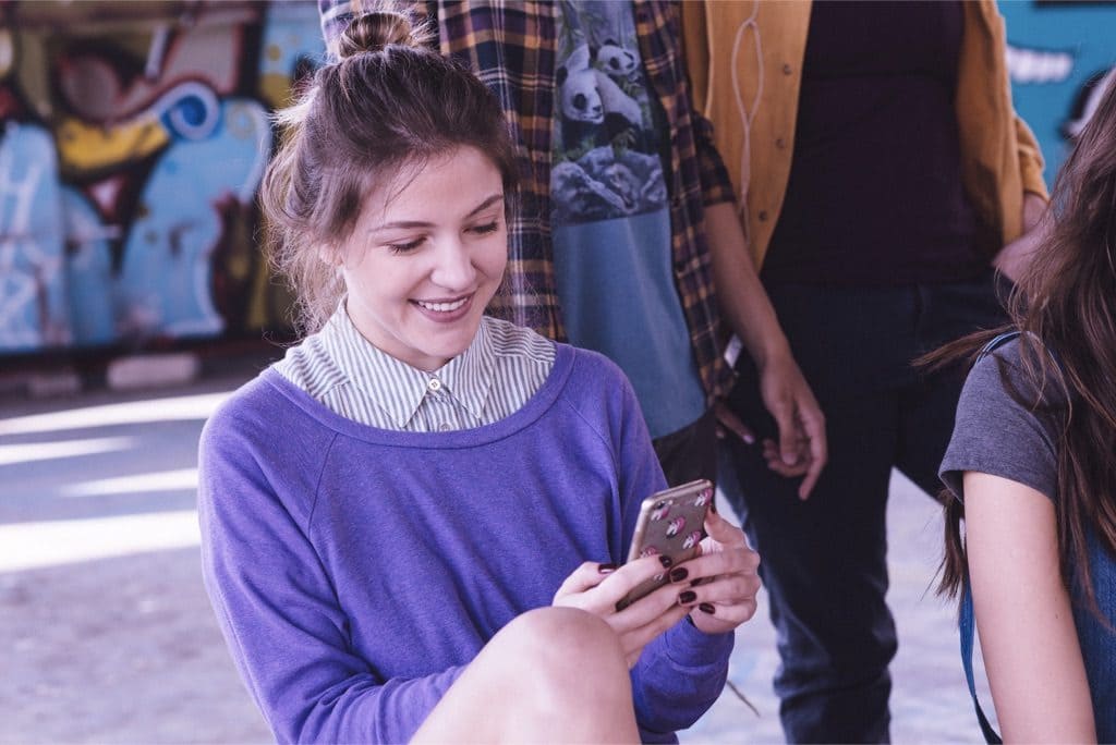 Chica con sweater morado mira un celular en donde aparece la tarjeta de crédito sin complicaciones