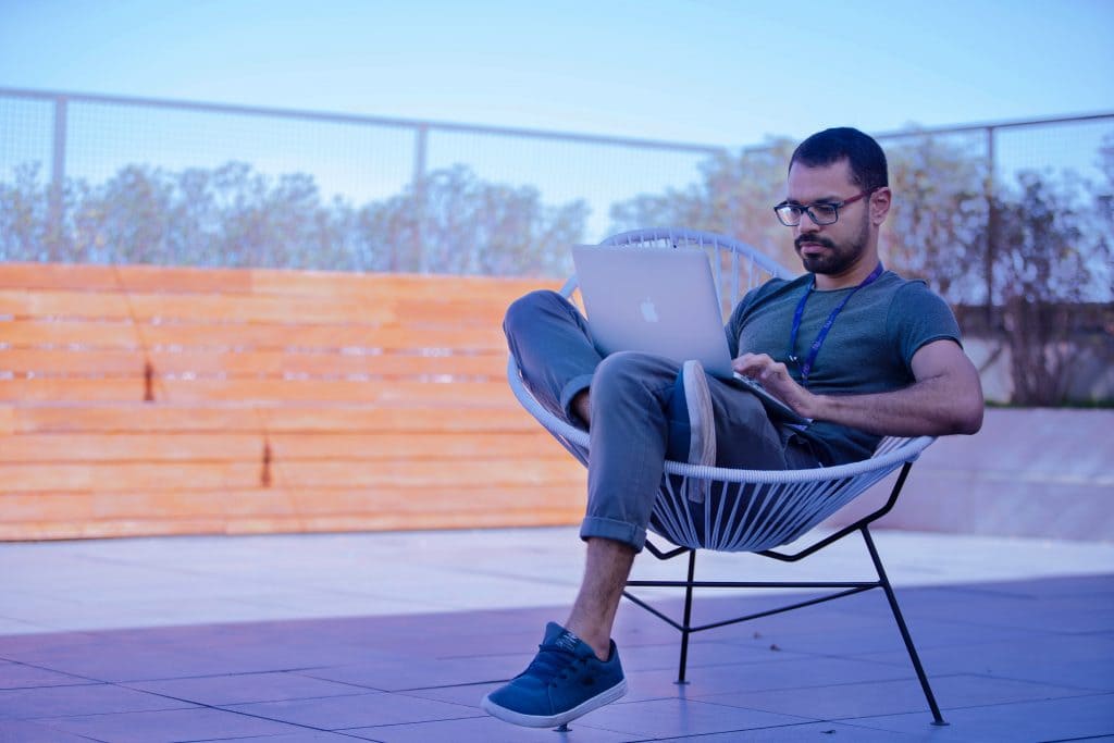 Chico  sentado en silla de terraza toma cursos gratuitos sobre finanzas personales en su computadora posrtatil