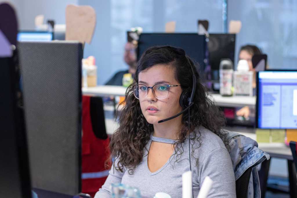 Chica de mediana edad, con auriculares y frente a una computadora atiene llamadas de servicio a cliente Nu