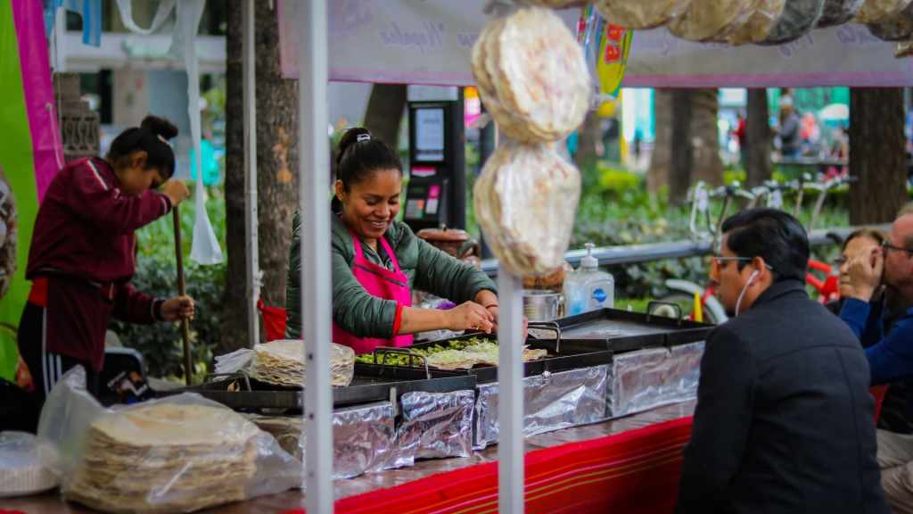Mujer mexicana con sudadera verde y mandil rosa atiende un puesto de comida callejera para cambiar su futuro