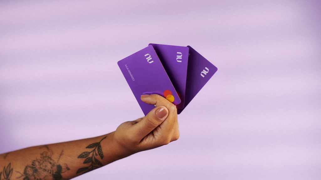 Una mano sostiene tres tarjetas moradas para simbolizar la reposición de la tarjeta de crédito Nu