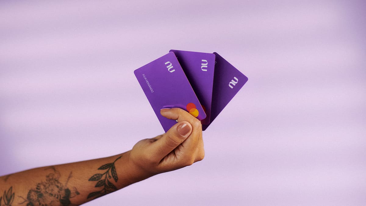 Una mano sostiene tres tarjetas moradas para simbolizar la reposición de la tarjeta de crédito Nu