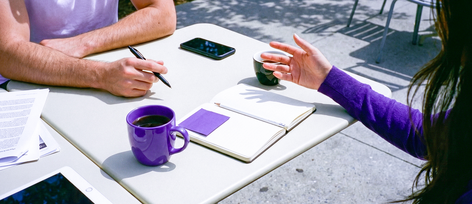 Dos personas analizando planes financieros en una mesa con notas y celular, ilustrando cómo una cuenta de ahorro te ayuda a organizar y planear tus metas.