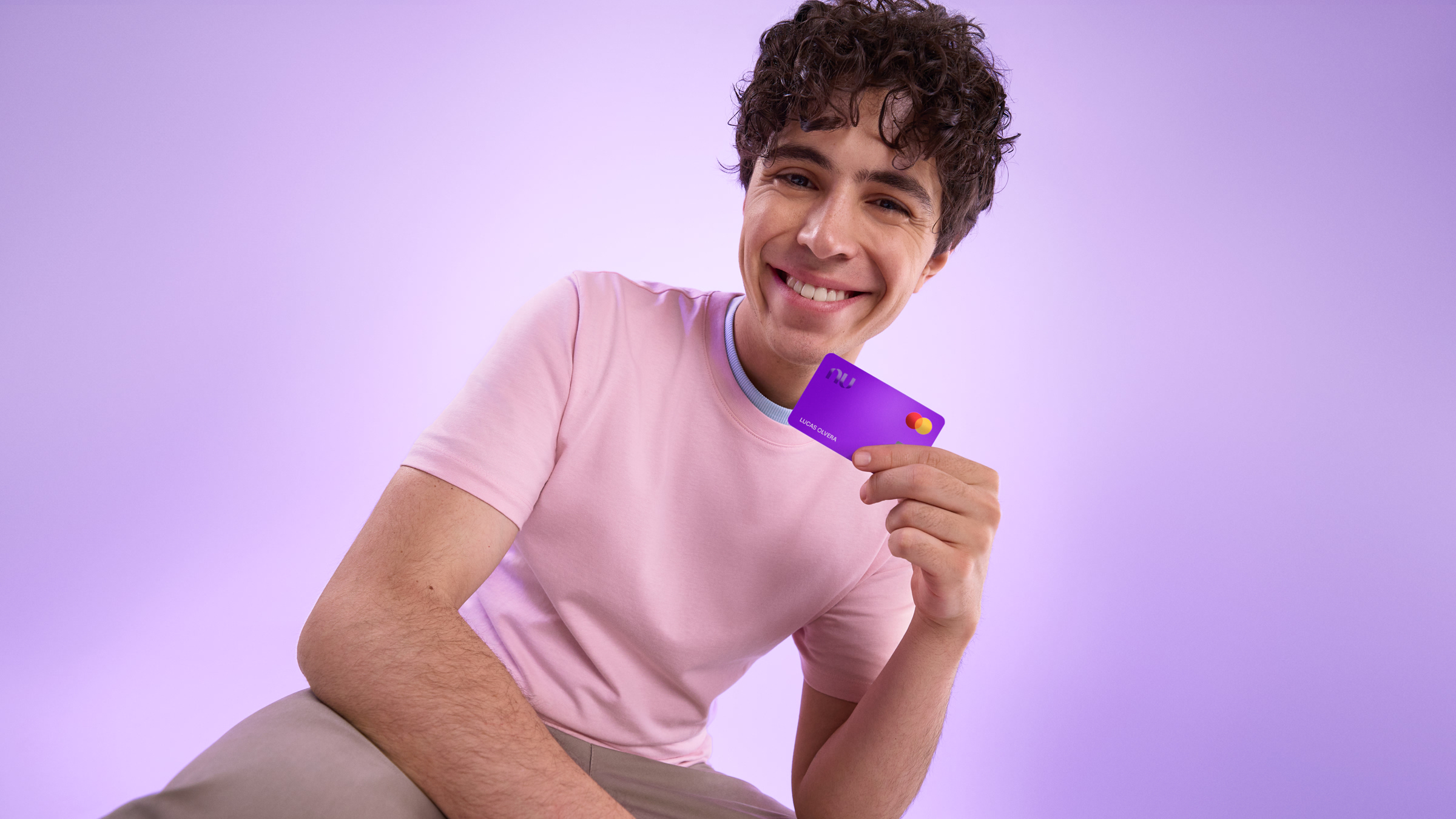 Joven sonriendo mientras sostiene su tarjeta morada de débito Nu, ilustrando lo fácil que es retirar efectivo de Cuenta Nu con tu tarjeta.