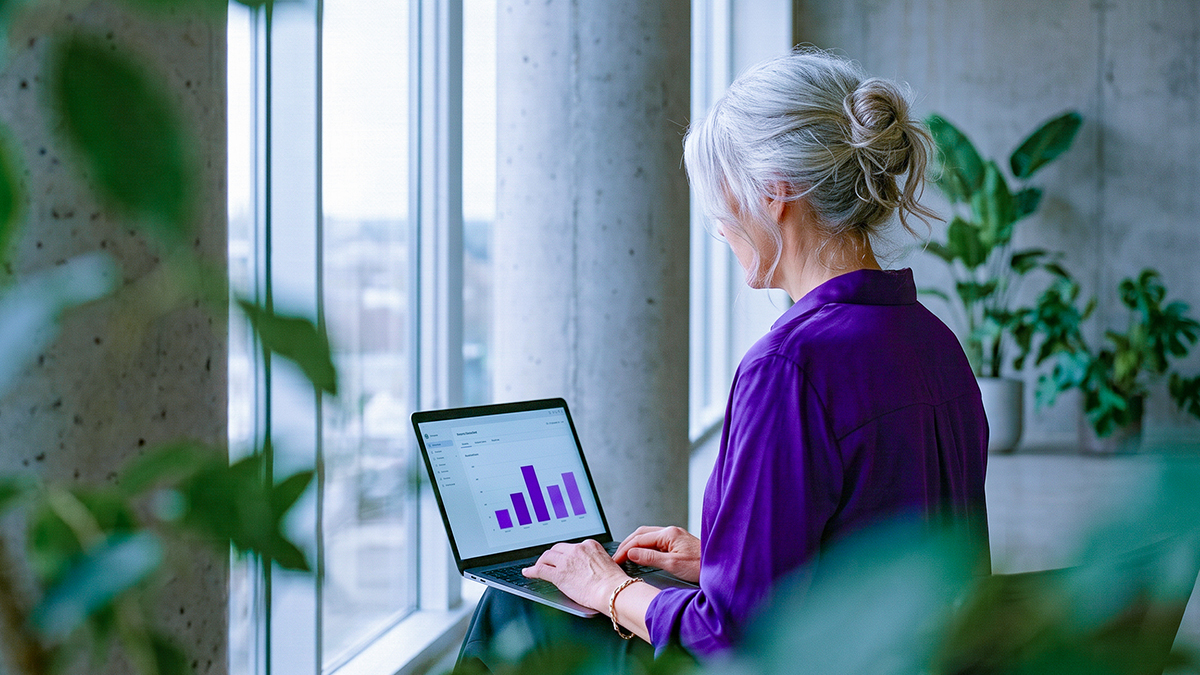 Persona analizando gráficos financieros morados en su laptop ante una ventana con vista a la ciudad, ilustrando cómo empezar con inversiones para principiantes: Cajitas Nu, CETES, fondos de inversión y ETFs desde $100.