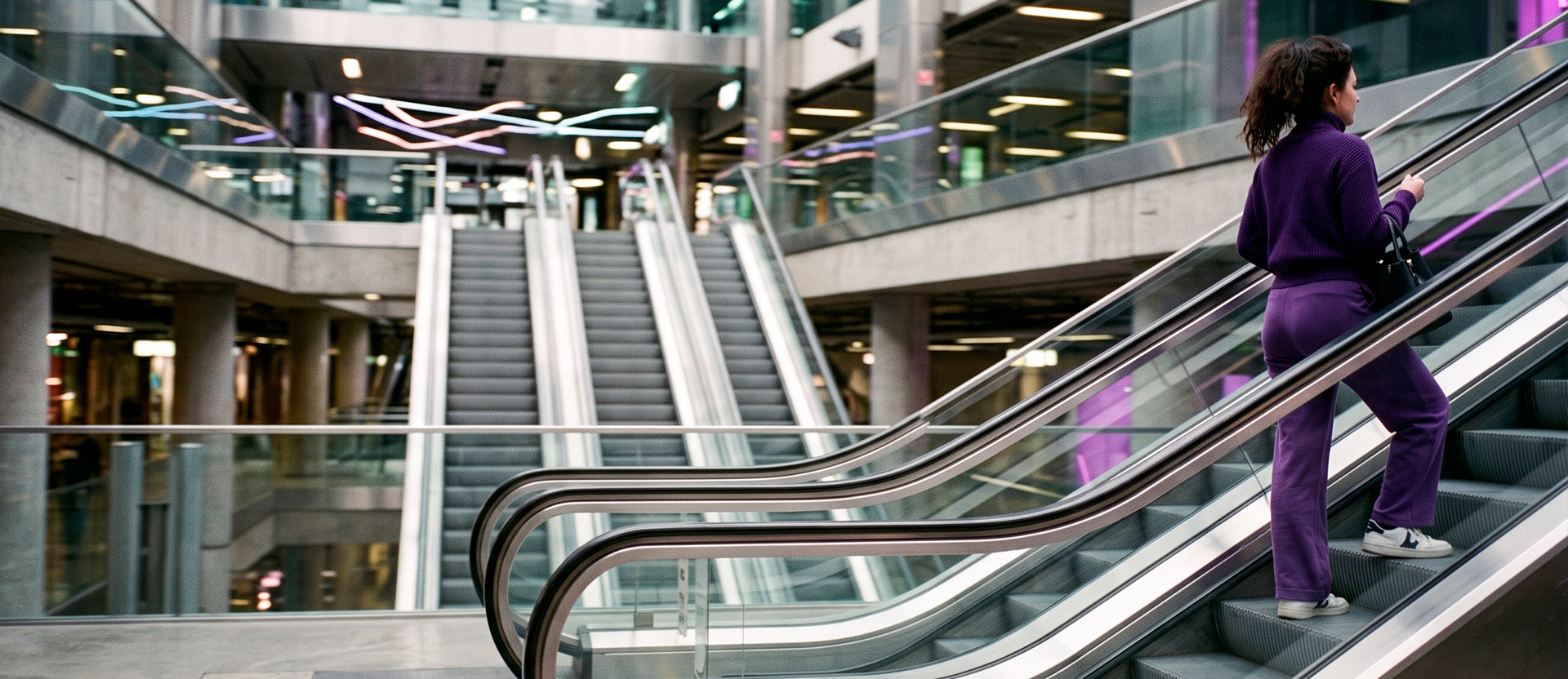 Mujer con conjunto morado subiendo por escaleras eléctricas en un centro comercial moderno.
