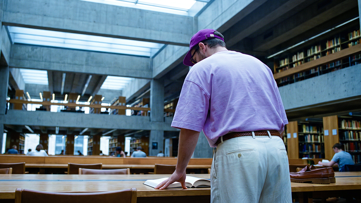 Persona con camisa morada estudiando en una biblioteca con libros y estanterías, ilustrando cómo entender qué es banca múltiple: la estructura legal y regulatoria de los bancos en México bajo supervisión de CNBV y Banxico.