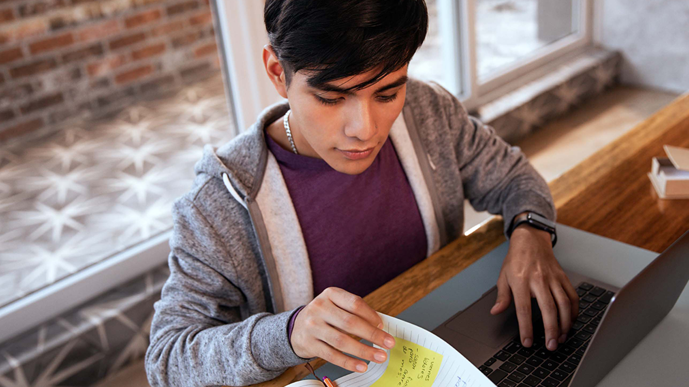 chico de tes morena en sus treintas vestido con sudadera gris y playera morada revisa hojas y su computadora para averiguar si es necesario pagar impuesto sobre el ahorro en México