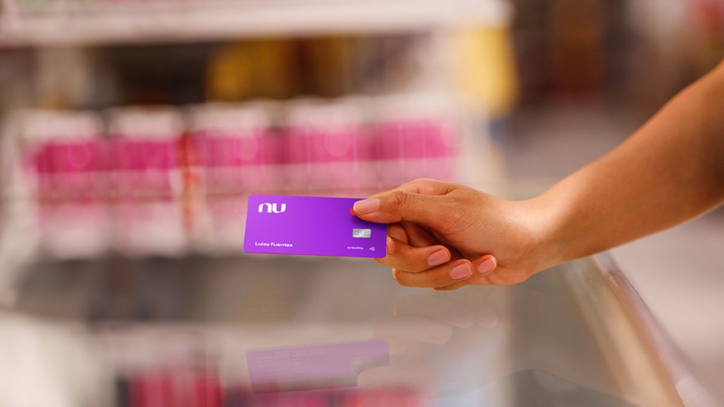 mano de mujer con tes canela extiende una Tarjeta Nu con límite de crédito cero color morada para recordar las ventajas de la tarjeta garantizada nu