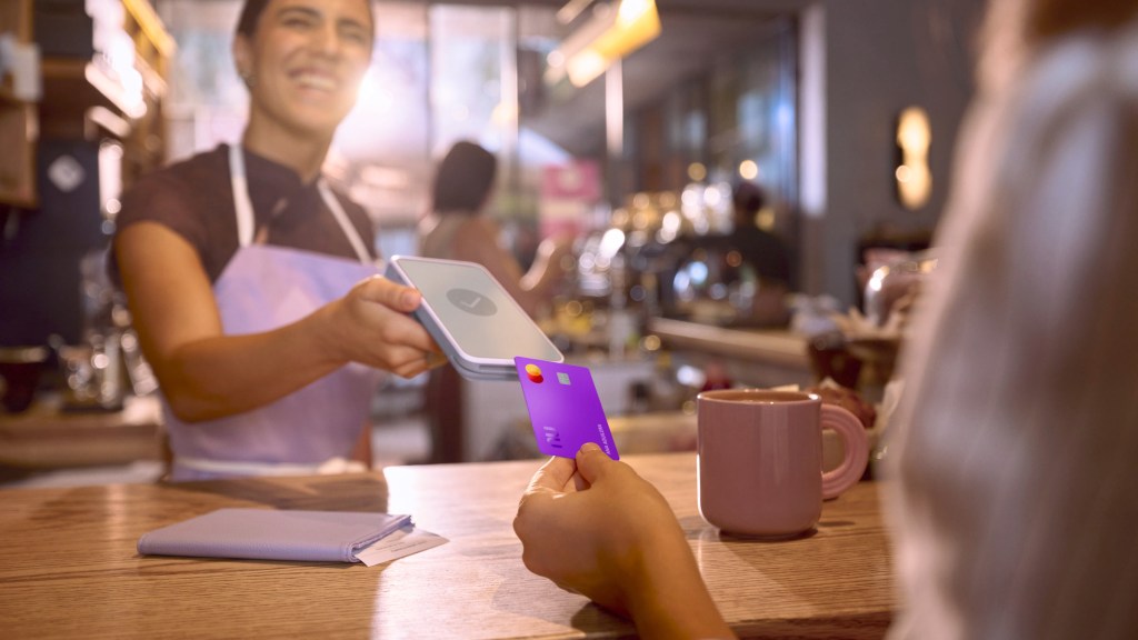 Persona usando su Tarjeta de Crédito Nu morada en una transacción comercial, ilustrando lo fácil que es usar una tarjeta de crédito internacional Nu en tus viajes.