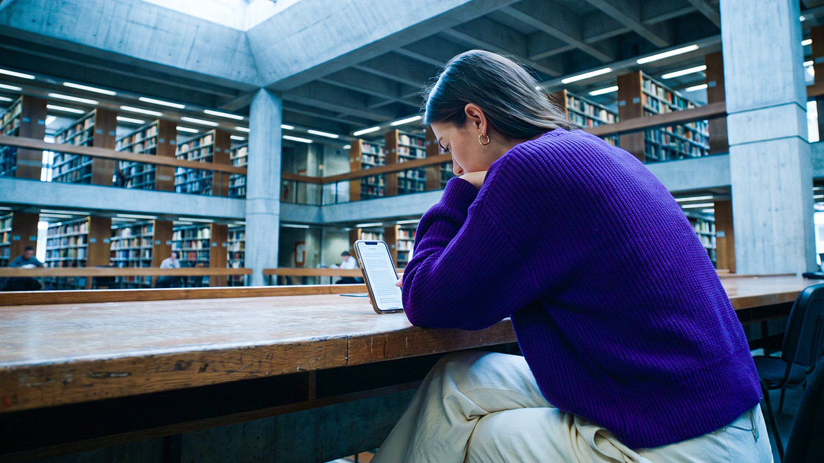 Persona usando su celular en una biblioteca, ilustrando por qué la protección de datos personales es importante en apps y dispositivos donde guardas información.