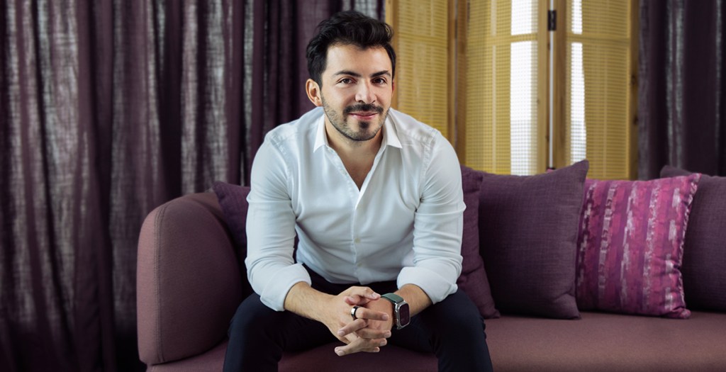 Alfredo Méndez sentado en un sillón color morado vistiendo una camisa blanca y un pantalón negro de vestir sonrie a la cámara para hablar de la tecnología que se utiliza en Nu