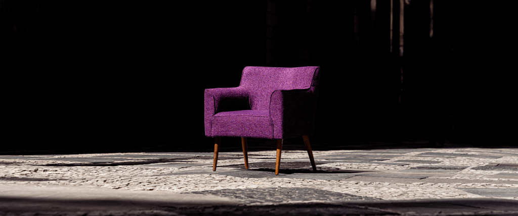 Una silla morada de terciopelo sobre una alfombra color marrón claro frente a una pared negra representa lo increíble de trabajar en Nu