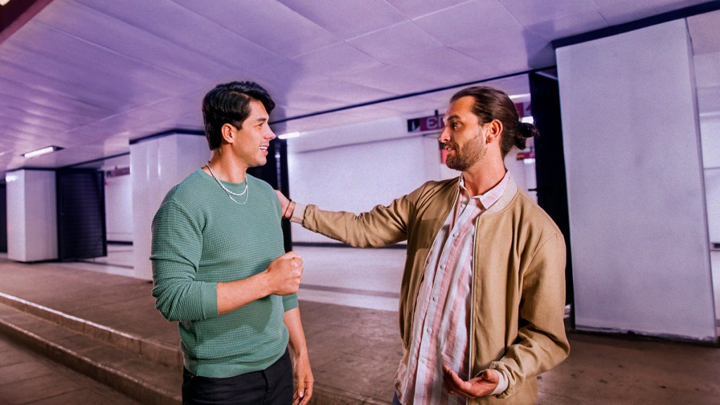 Header_cobrardeuda Dos hombres jóvenes de edad mediana hablan mientras uno le toca el hombro al otro para saber cómo cobrar una deuda, ambos visten ropa relajada el colores beige rosa y verde, se encuentran en un estacionamiento