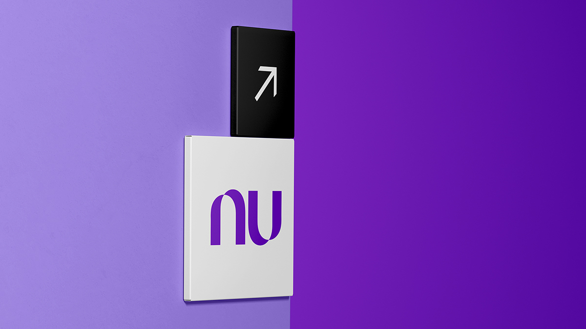 Una señalética de Nu en una pared morada sostiene un indicador de flecha que apunta hacia arriba para anunciar que Nu Holdings Ltd. reporta sus resultados financieros del tercer trimestre del 2024