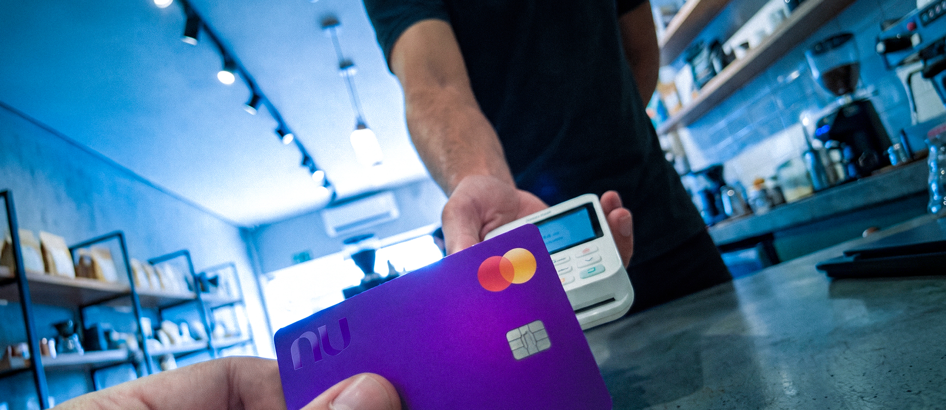 Persona pagando con su Tarjeta de Crédito Nu en una terminal de pago en un comercio, ilustrando qué hacer cuando te cobran comisión por pagar con tarjeta: es ilegal y tienes derechos.