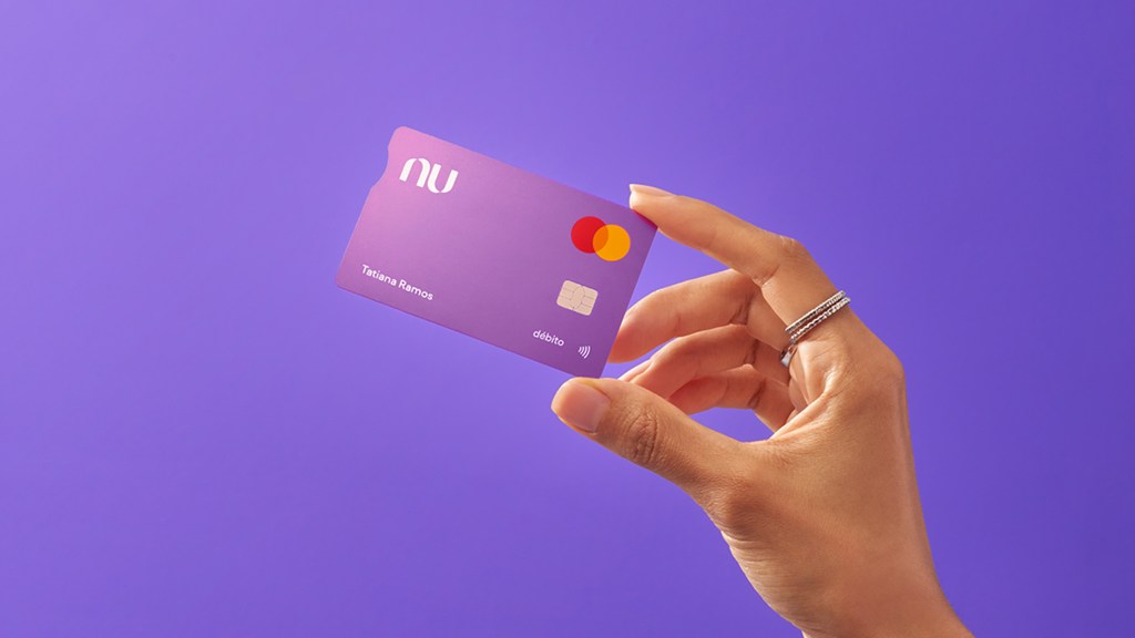 mano sostiene tarjeta de crédito nu ientras se hace un pequeño reflejo en la esquina de la tarjeta morada