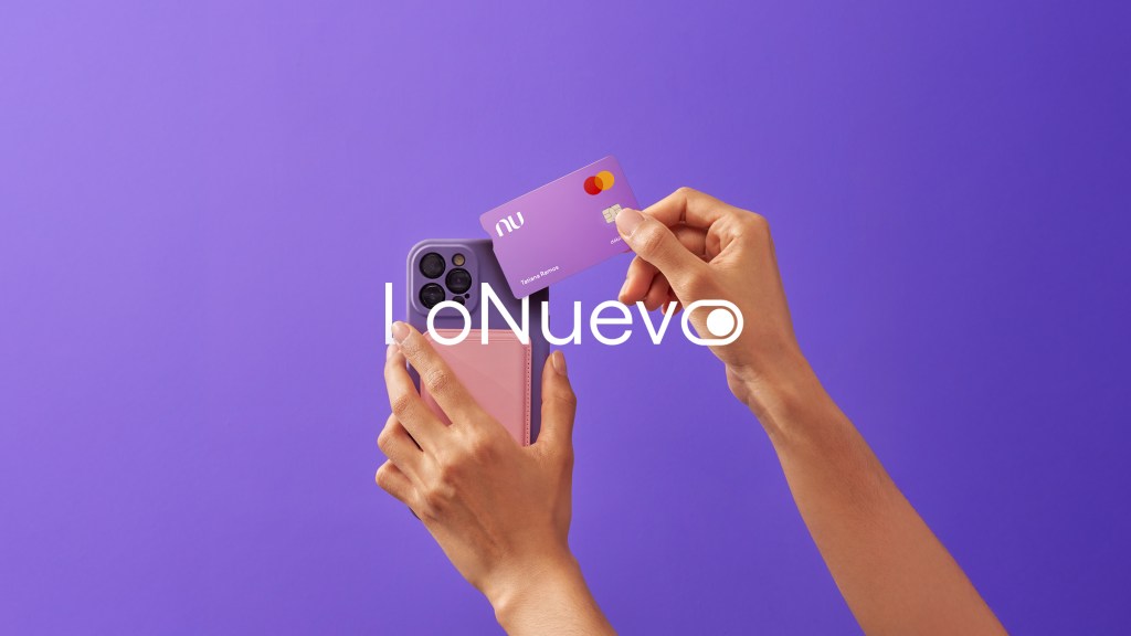 Header-Lo Nuevo Di Una mano sostienes una Tarjeta de crédito nu mientras la otra sostiene un celular frente a un fondo morado para advertir de Nu en diciembre