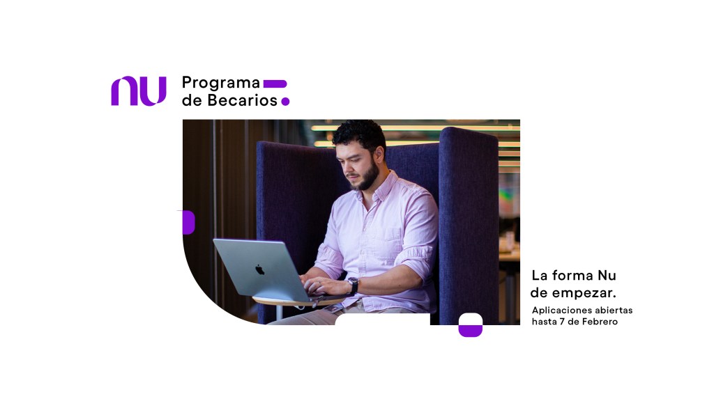 Un chico becario de edad mediana con una camisa color lila escribe en una computadora abierta dentro de las oficinas de Nu México en un escritorio de madera clara