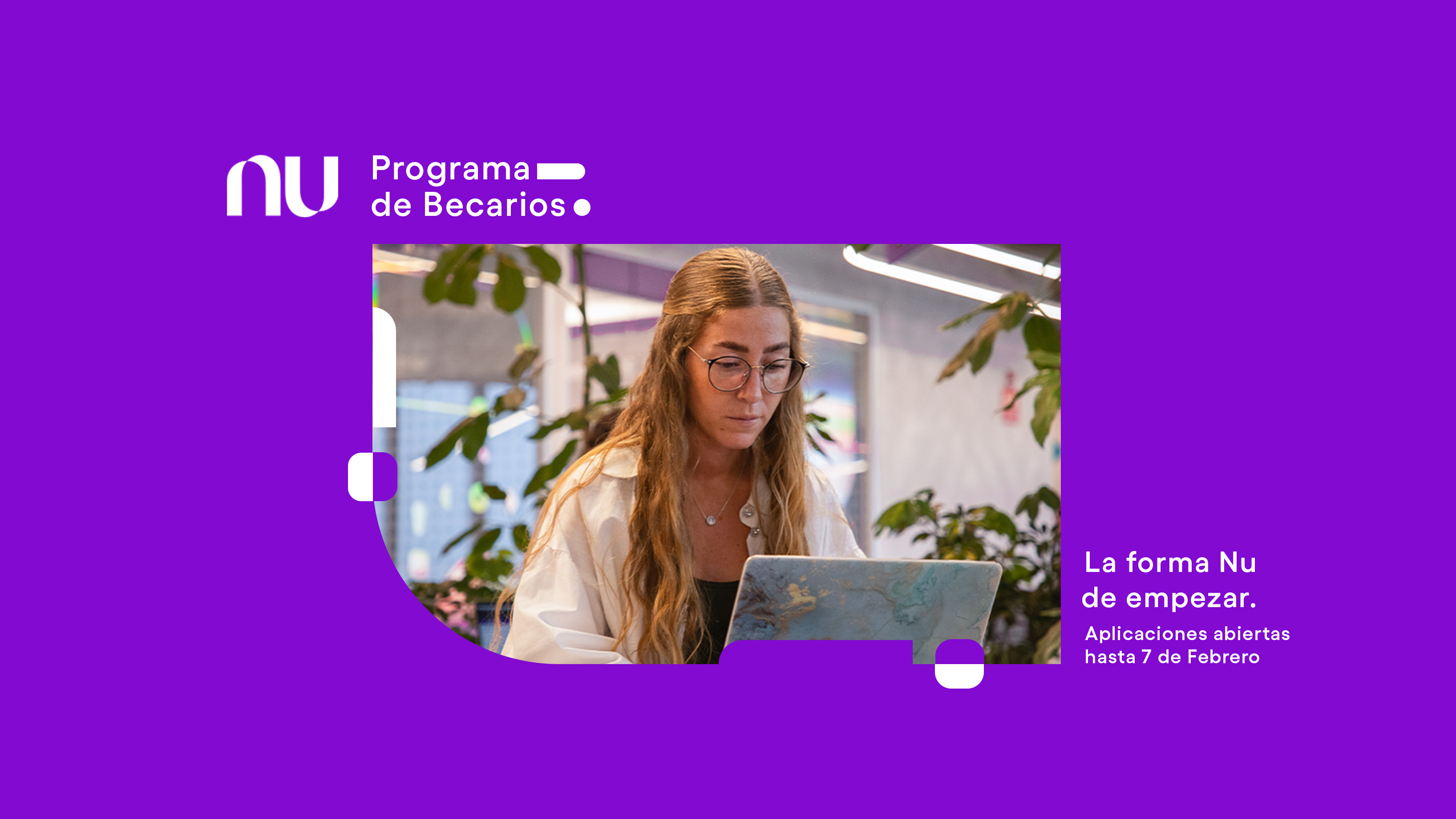 Una chica joven con cabello rubio y chamarra blanca mira la pantalla de una computadora en la oficinas de nubank mientras lee la entrada sobre el programa de becarios en el blog nu