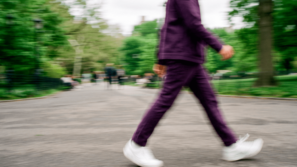 Persona caminando de forma relajada en un parque, con traje deportivo morado y tenis blancos, representando el control y la tranquilidad financiera al usar los Meses Sin Intereses.