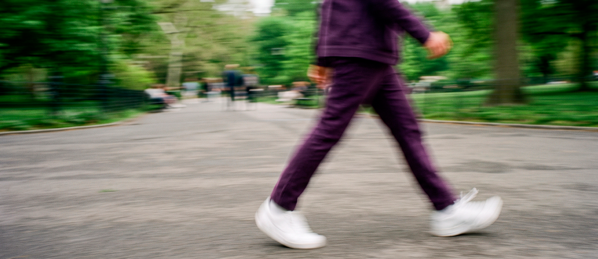 Persona caminando de forma relajada en un parque, con traje deportivo morado y tenis blancos, representando el control y la tranquilidad financiera al usar los Meses Sin Intereses.