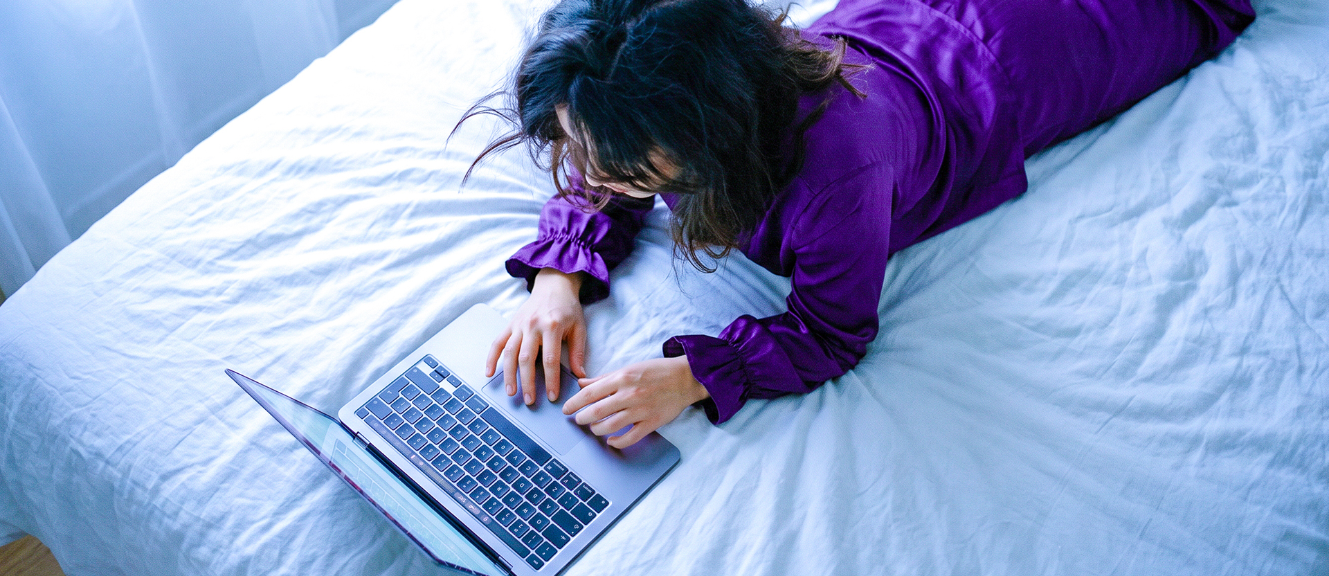 Persona usando su laptop en la cama con camisa morada, ilustrando cómo checar tu buró de crédito en línea de forma fácil para tomar control de tu historial crediticio.