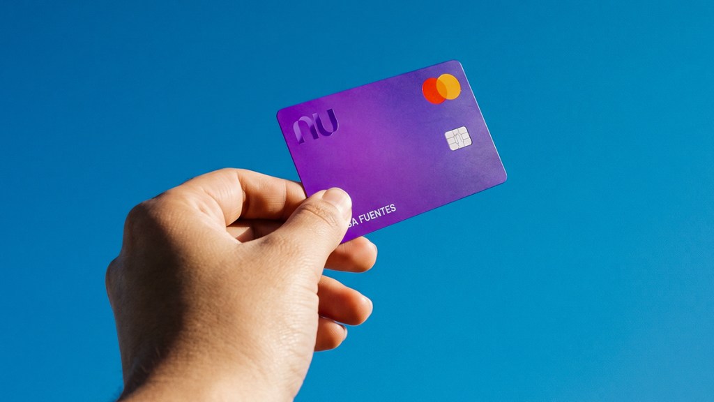 Mano sosteniendo su Tarjeta de Crédito Nu morada contra fondo azul, ilustrando cómo pagar una tarjeta de crédito completa antes de la fecha límite para evitar intereses.