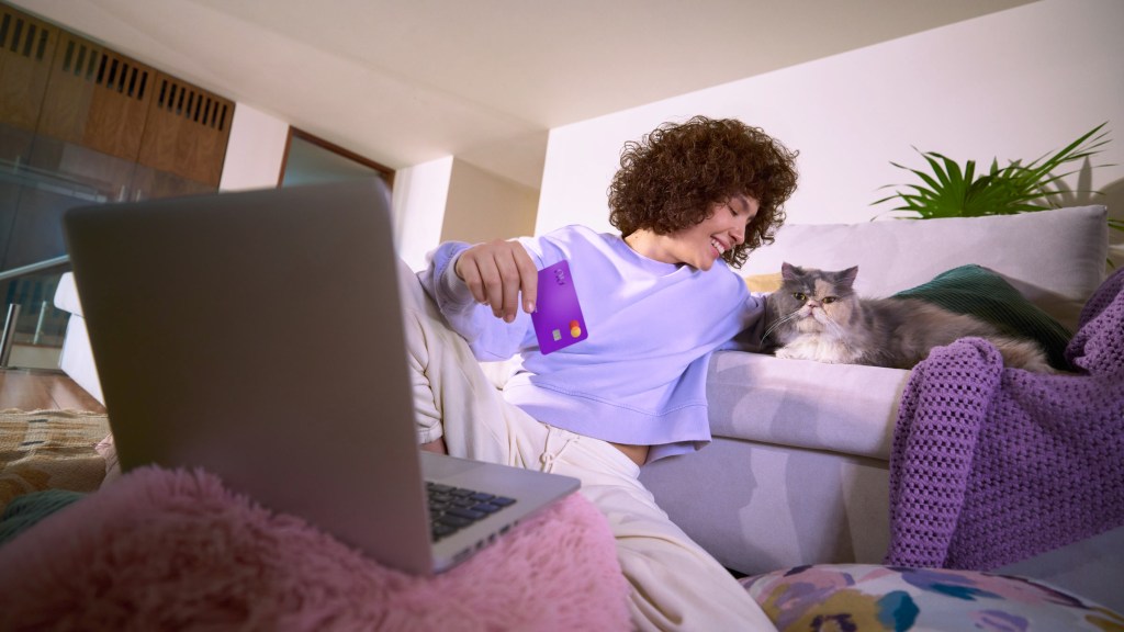 Mujer cómoda en su sofá con su laptop y tarjeta morada, representando la tranquilidad de transferir saldo entre tus cuentas Nu.