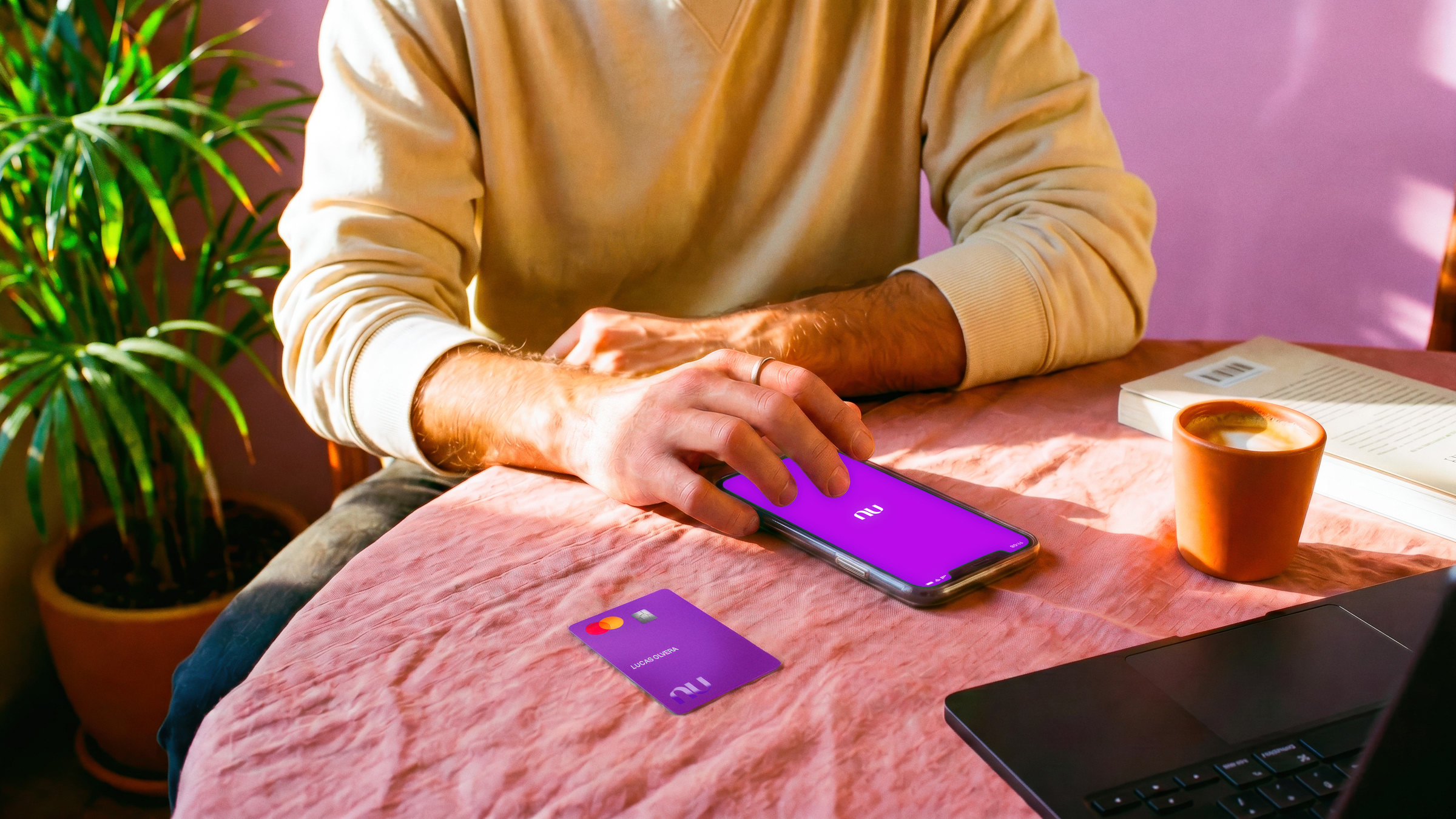 Persona sosteniendo su celular con la app Nu abierta, junto a su tarjeta morada Nu sobre una mesa.