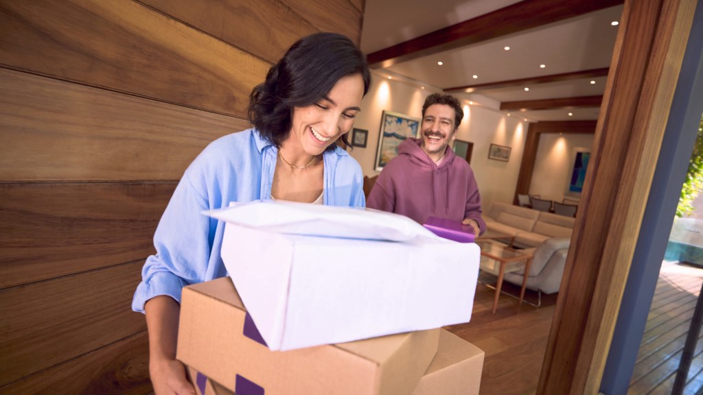como-retirar-rendimientos-cajitas-nu_Header Pareja sonriente recibiendo paquetes en casa, reflejando cómo puedes usar tu dinero al retirar los rendimientos de tus Cajitas Nu.