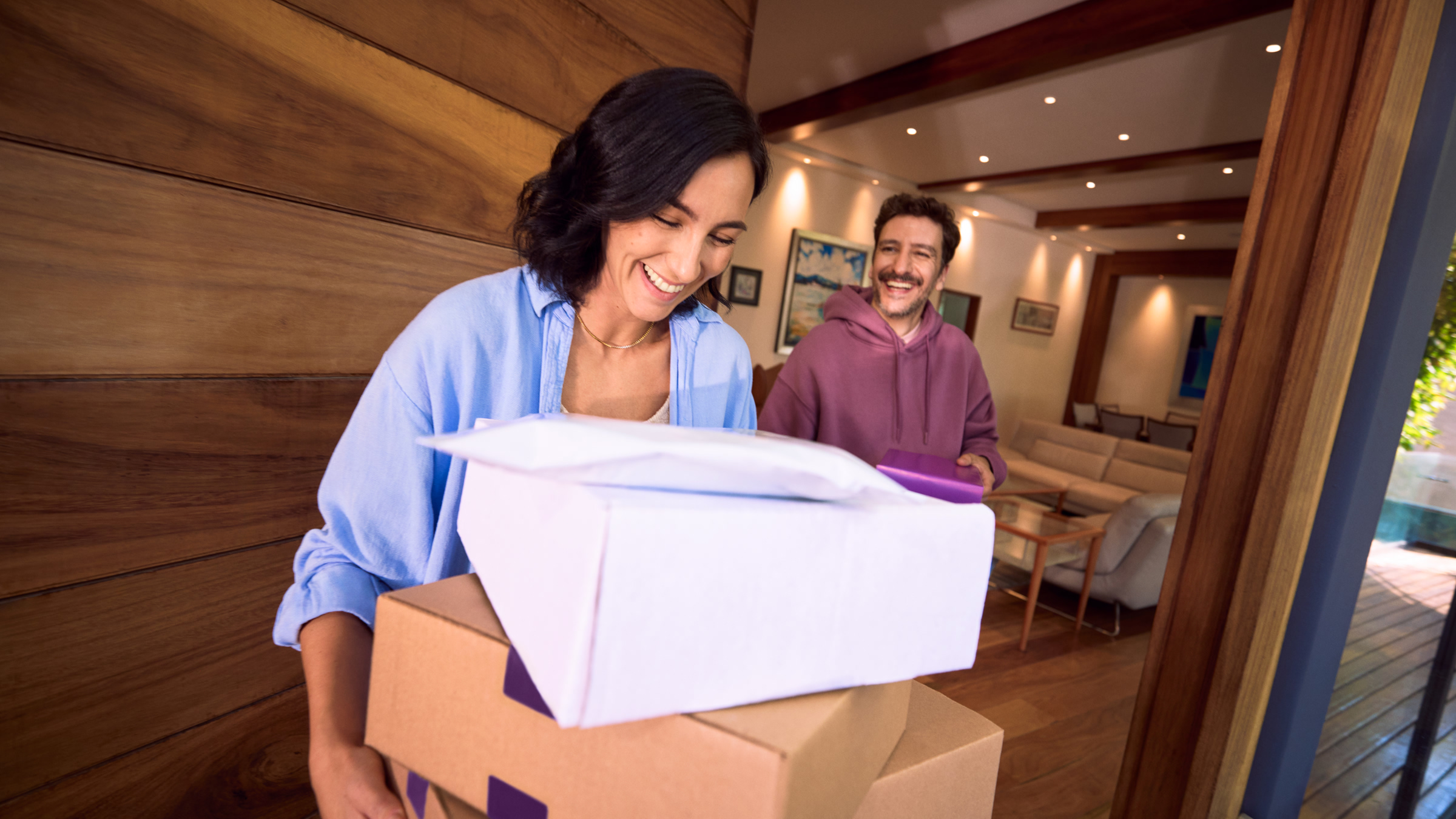 Pareja sonriente recibiendo paquetes en casa, reflejando cómo puedes usar tu dinero al retirar los rendimientos de tus Cajitas Nu.