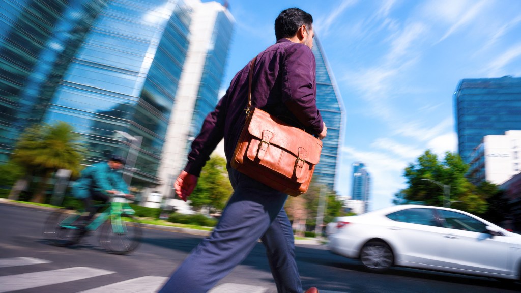 Hombre caminando con determinación por la ciudad, reflejando la agilidad de usar tu TDC Nu para disponer de efectivo y transferir cuando surge un imprevisto.
