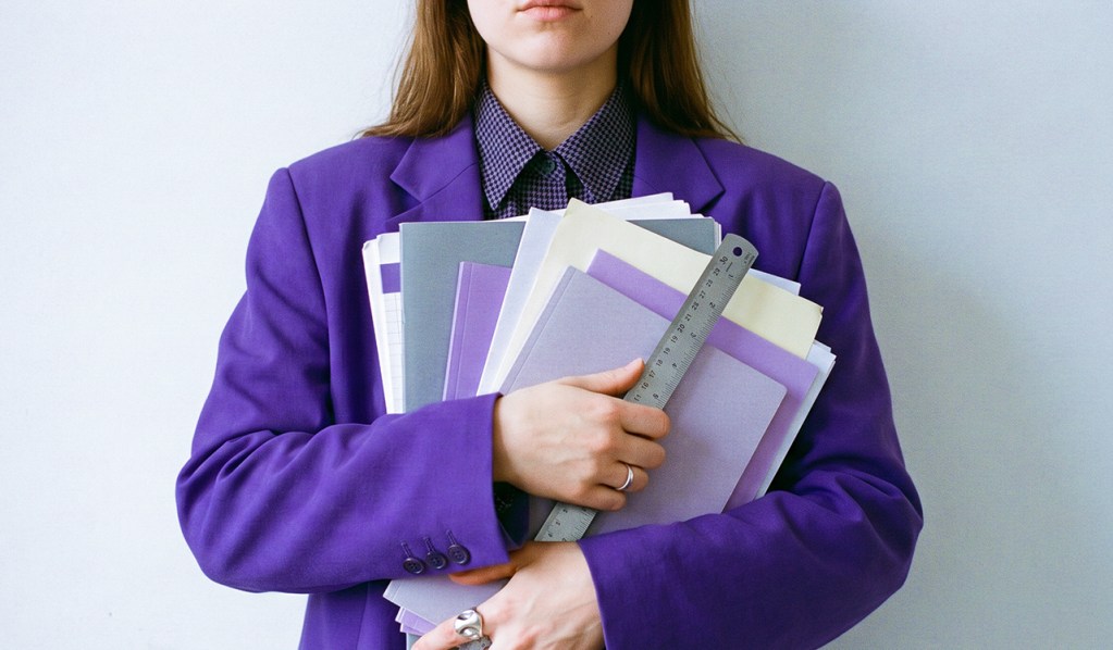 Persona en traje morado sosteniendo múltiples documentos y carpetas, ilustrando el complejo proceso de cómo se obtiene licencia bancaria en México con requisitos de capital y gobierno corporativo.