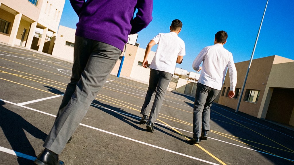gasto-regreso-a clases_Header Tres estudiantes corriendo en un patio escolar soleado, viendo hacia atrás con libertad y energía.