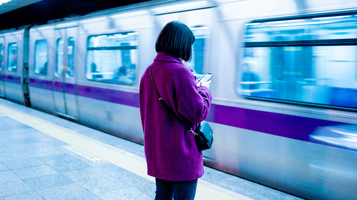 Persona revisando su celular en una estación de metro, ilustrando que ahora que Nu es banco, no necesitas hacer trámites y todo sigue igual en tu vida cotidiana.