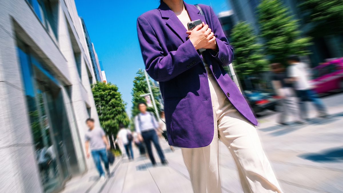 Persona con blazer morado sosteniendo su celular en una calle urbana, rodeada de gente y edificios.