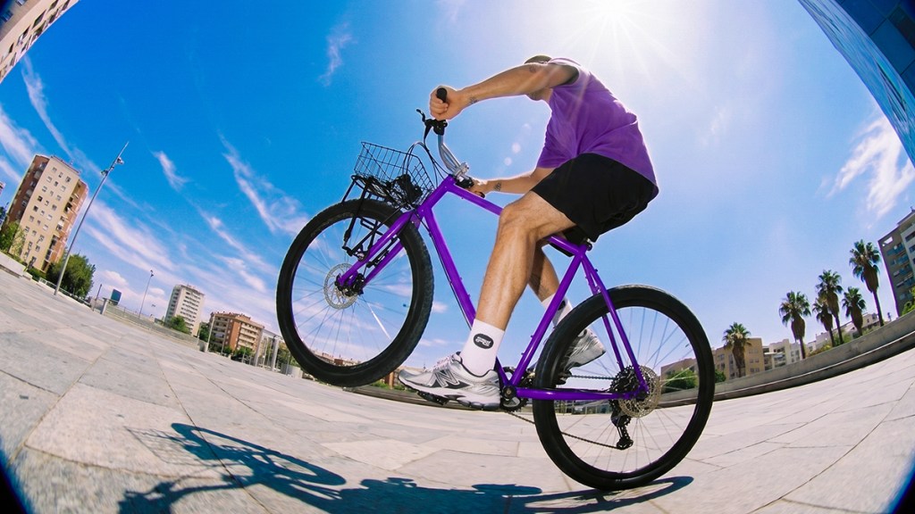 Persona en bicicleta morada avanza con constancia por una plaza soleada, una metáfora de cómo aumentar tu línea de crédito paso a paso con buenos hábitos.