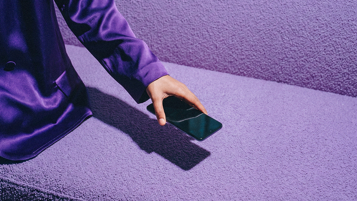 Mano sosteniendo un celular morado Nu contra fondo púrpura, ilustrando el manifiesto Nubank: simplificar dinero sin trámites, filas ni letras chiquitas, dándote control total en tu mano como banco.