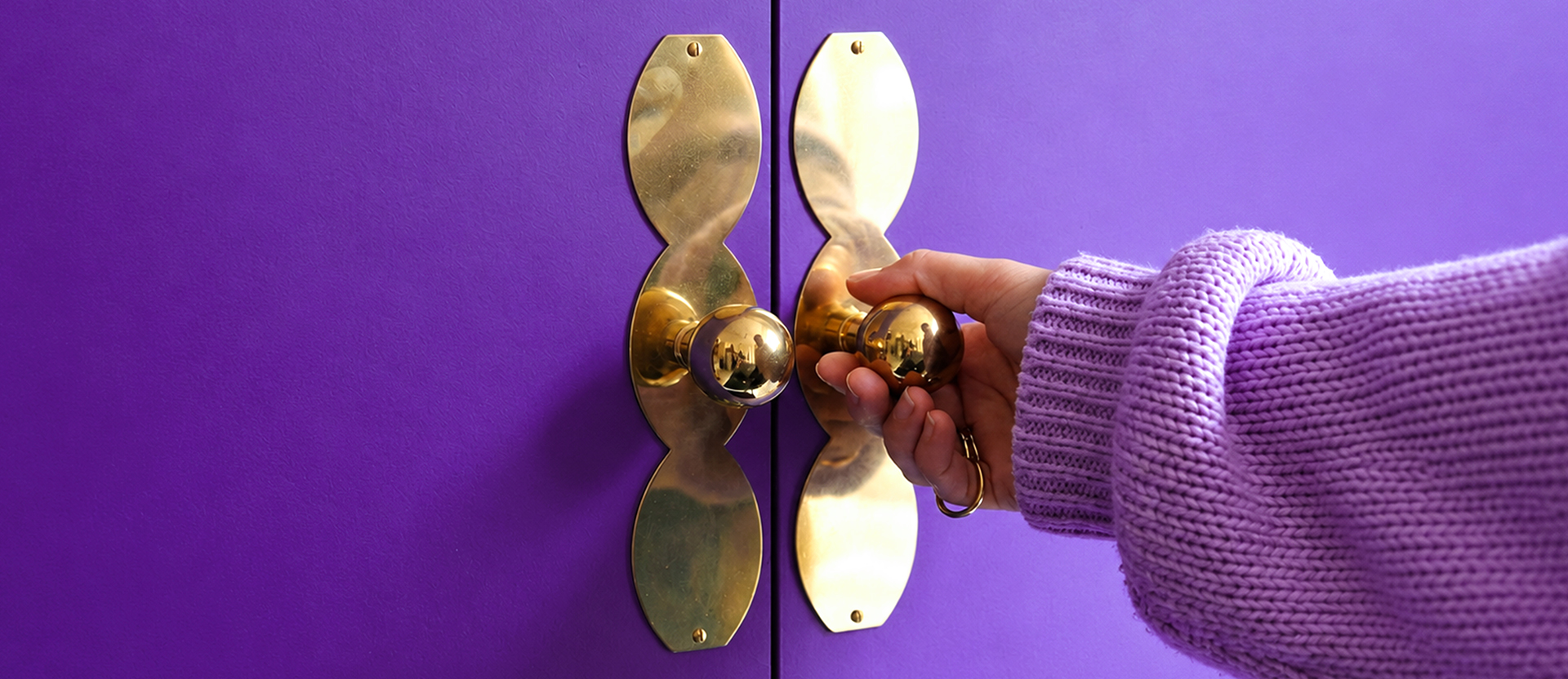 Mano con suéter morado abre unas puertas moradas con manijas doradas, una metáfora de cómo organizar tus finanzas en la app Nu con unos pocos ajustes.