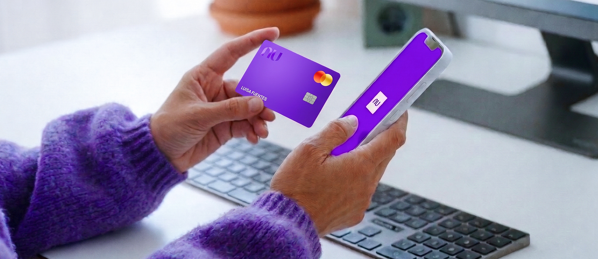 Manos con suéter morado sostienen una tarjeta Nu y un celular con la app abierta, para elegir entre tarjeta de débito virtual vs física según cada compra.