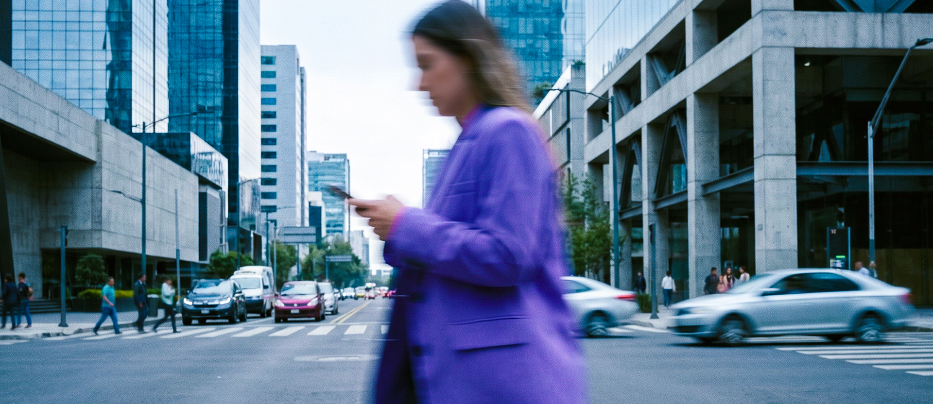 Mujer con blazer morado cruza una calle mientras revisa su celular, una escena cotidiana donde conocer los tipos de phishing ayuda a evitar fraudes.