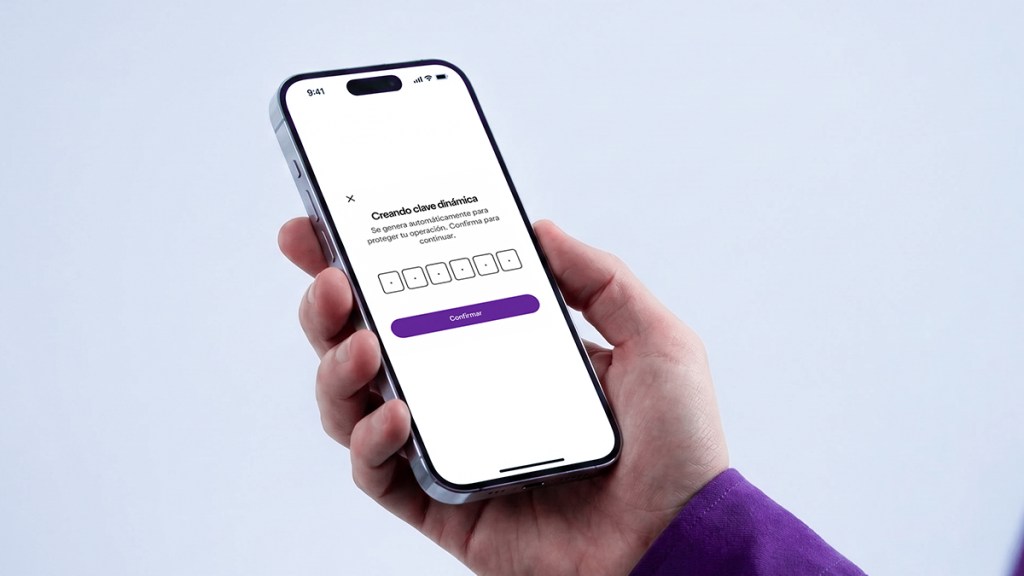 Mano sosteniendo un celular mostrando la pantalla de “Creando clave dinámica” con campos para código de seguridad dinámico y botón morado Confirmar, ilustrando cómo funciona el token de seguridad Nu.